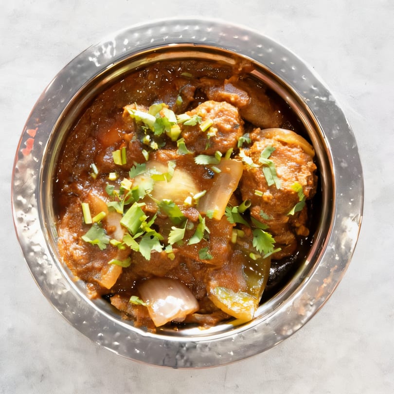 Saffron Indian Cuisine's chicken chili, a dark stew with chicken, onions, and green herbs in a silver bowl.