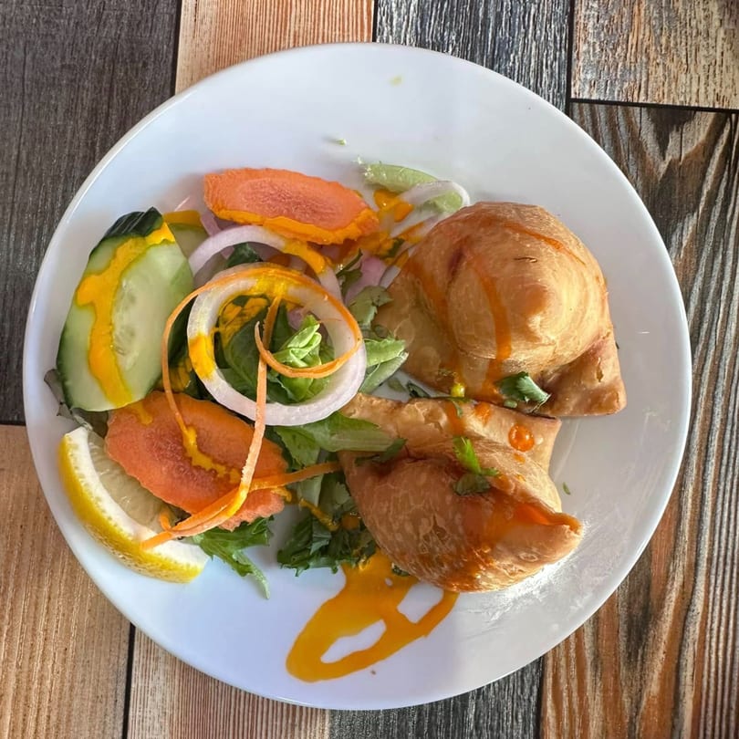 Two golden-brown samosas with a side salad of cucumber, carrots, onions, lettuce, and lemon.