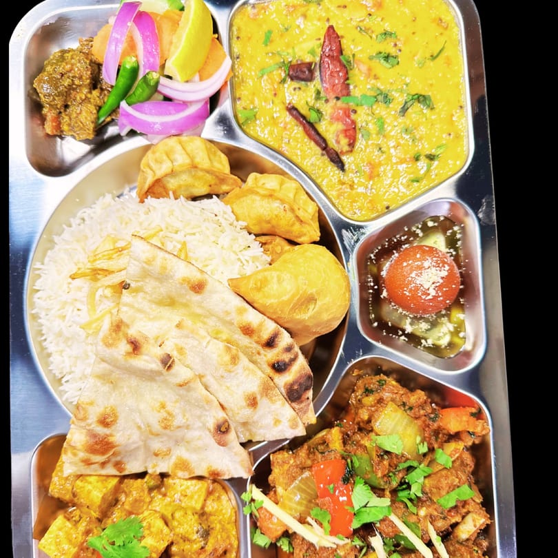 A Saffron Indian Cuisine thali with rice, naan, curries, gulab jamun, and fried dumplings.