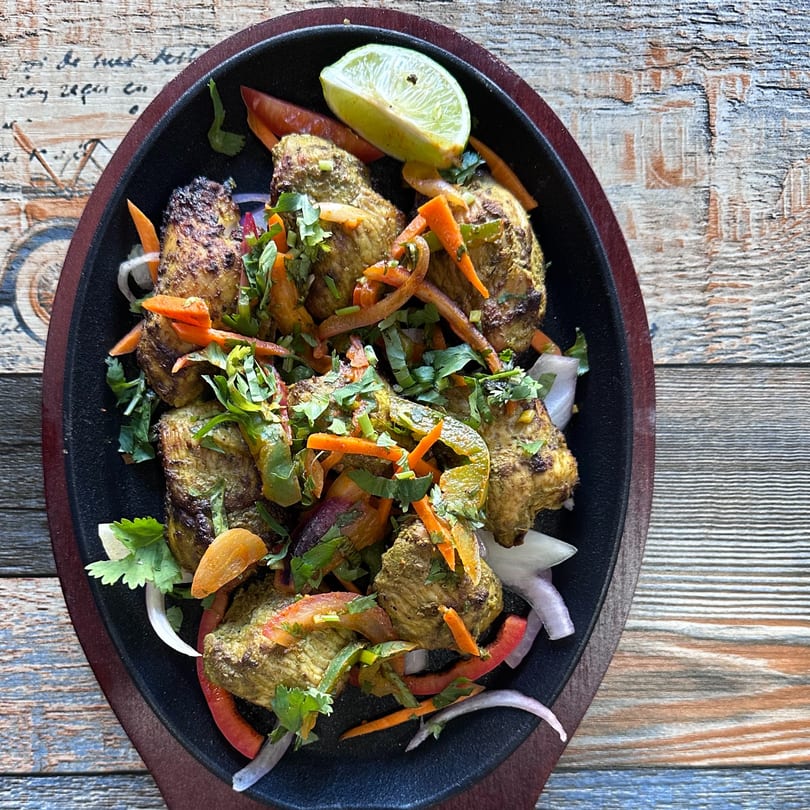 Saffron Indian Cuisine's chicken tikka, garnished with cilantro, onions, peppers, and a lime wedge.