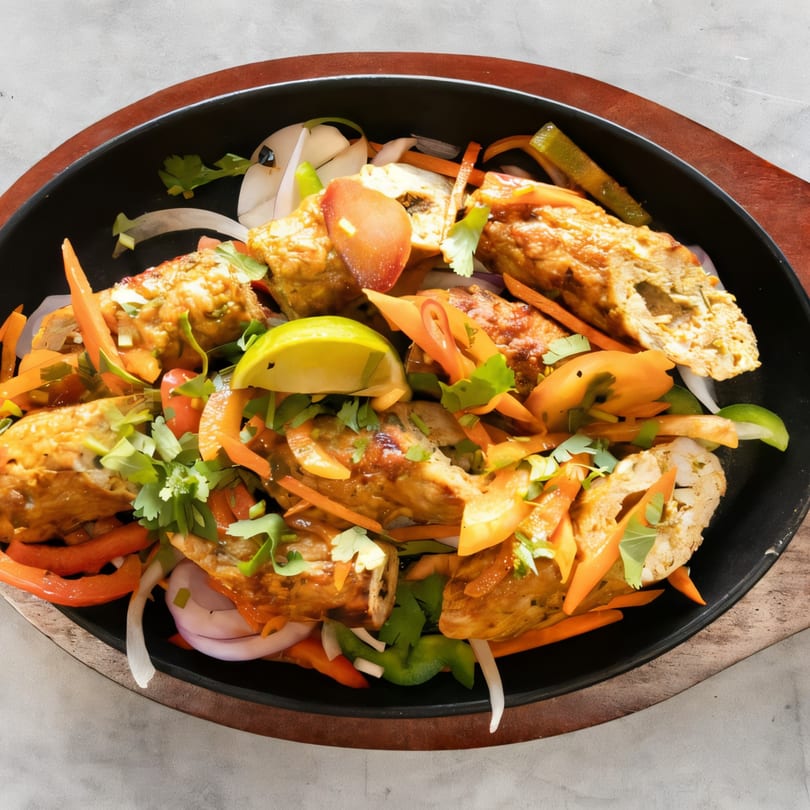 Saffron Indian Cuisine's seekh kebab, garnished with fresh vegetables and a lime wedge, served on a hot plate.