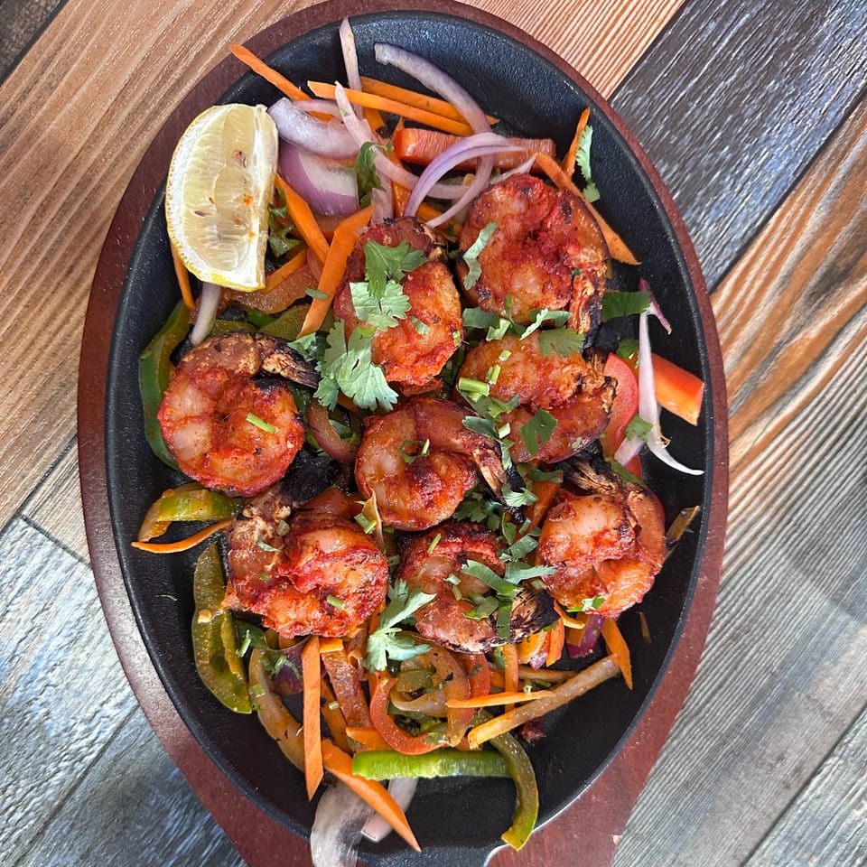 Saffron Indian Cuisine's sizzling tandoori shrimp with bell peppers, onions, carrots, and a lemon wedge.