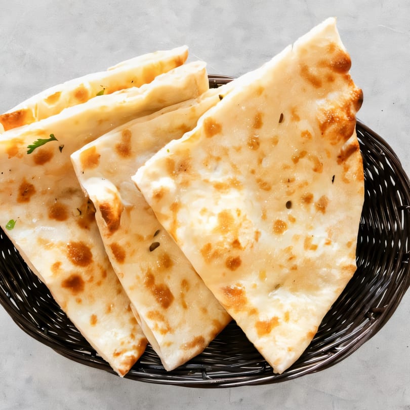 A basket of freshly baked Indian naan bread, golden brown and garnished with herbs.