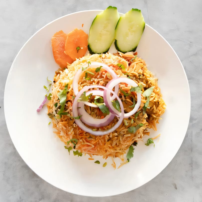 Saffron Indian Cuisine's chicken biryani, garnished with red onion, cilantro, carrots, and cucumber slices.
